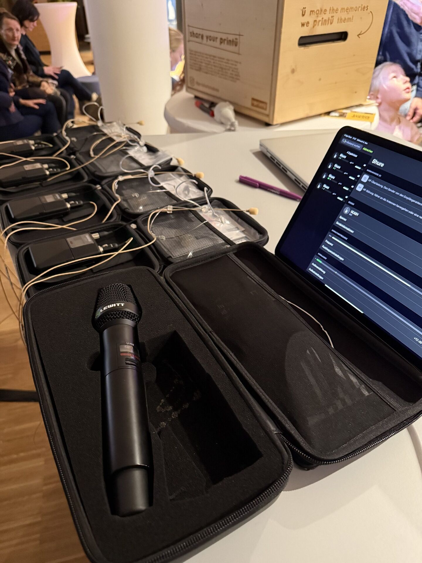 LEWITT-Handsender im offenen Koffer, daneben mehrere Taschensender mit Lavalier-Mikrofonen und ein iPad zum Funkstrecken-Management