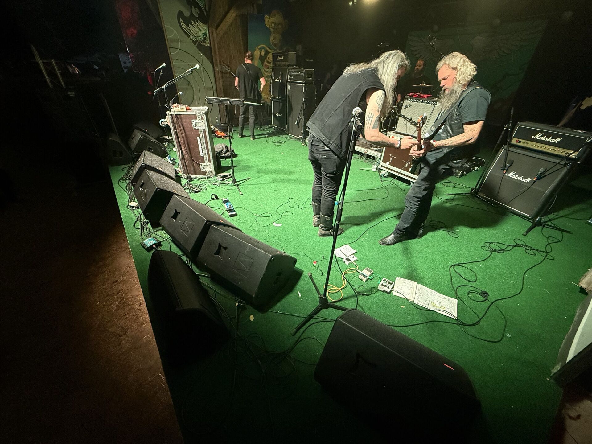 Kleine Clubbühne mit grünem Teppich von oben gesehen, zwei Musiker mit Gitarren, Marshall-Verstärker und Monitor-Wedges am Bühnenrand