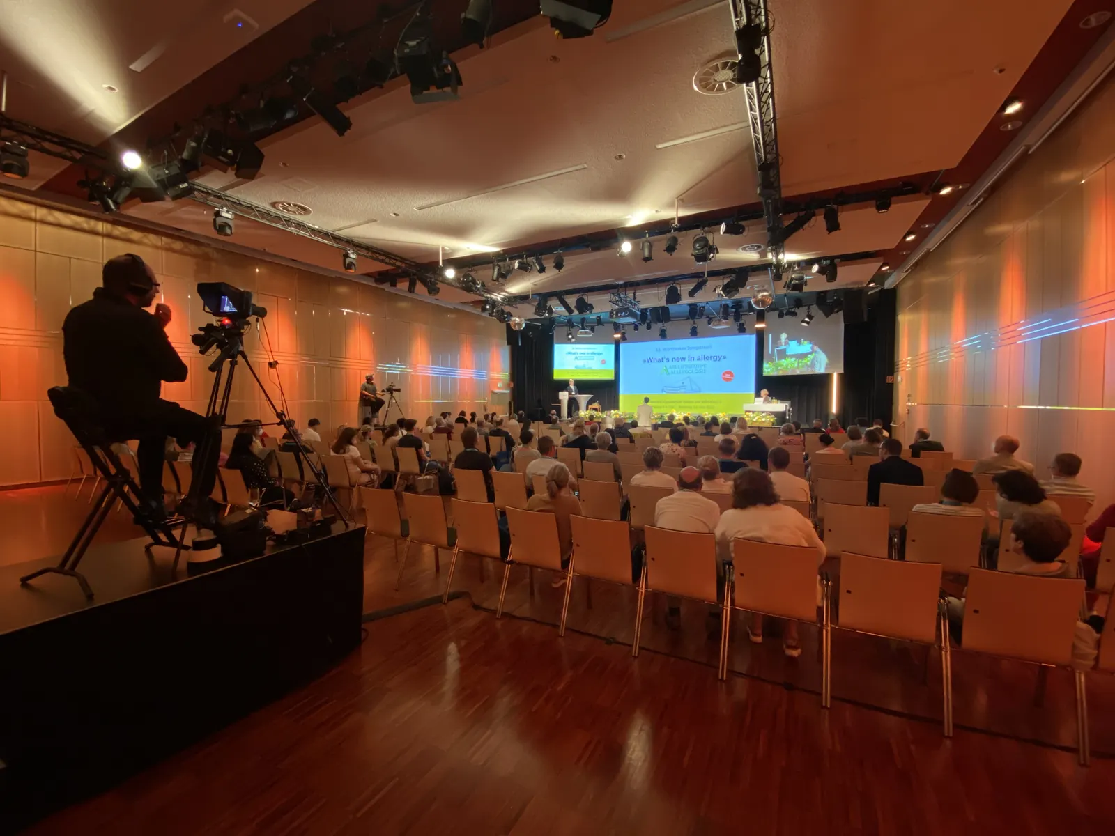 Konferenzaufzeichnung: Kamera auf Stativ vor vollbesetztem Saal